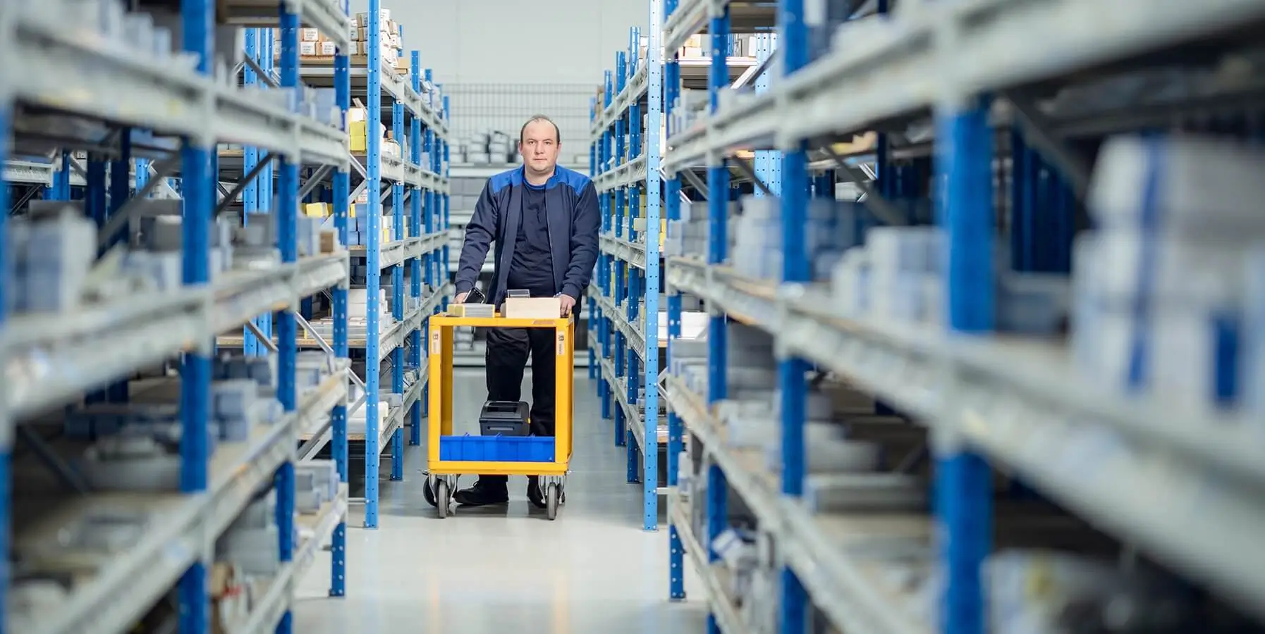 Een groot en geordend magazijn waar een medewerker een bestelling aan het picken is.